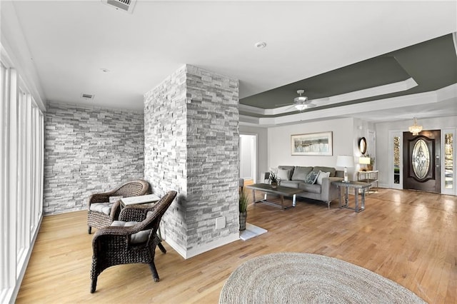 living area featuring a healthy amount of sunlight, a ceiling fan, a tray ceiling, and wood finished floors