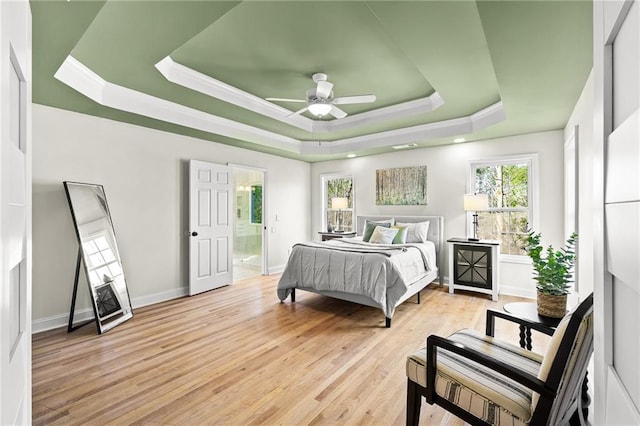 bedroom featuring a tray ceiling, baseboards, light wood-type flooring, and ornamental molding