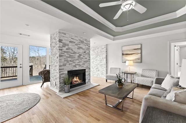 living area featuring ornamental molding, wood finished floors, a fireplace, a raised ceiling, and ceiling fan