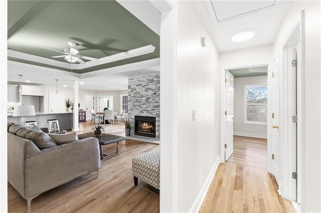 living area with a raised ceiling, light wood-style flooring, a fireplace, baseboards, and ceiling fan