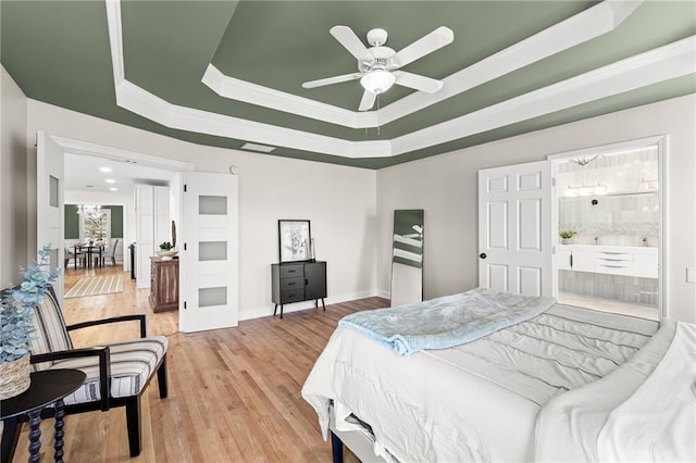 bedroom with baseboards, a tray ceiling, light wood-style flooring, ensuite bathroom, and crown molding