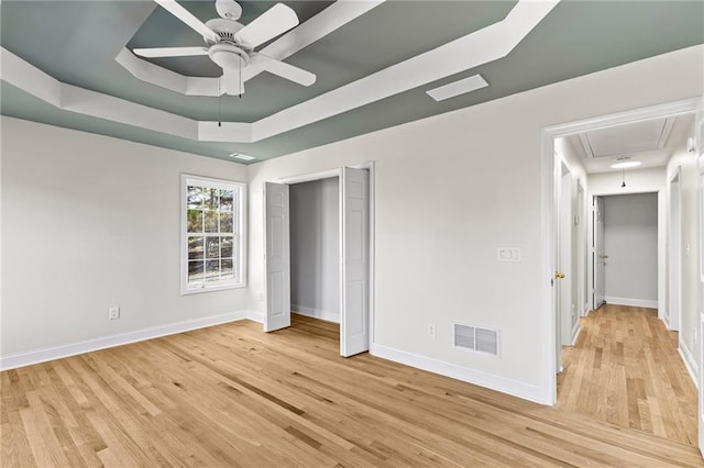 unfurnished bedroom featuring visible vents, a raised ceiling, light wood-style flooring, baseboards, and attic access