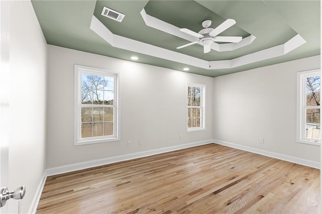 empty room featuring a tray ceiling, baseboards, visible vents, and wood finished floors