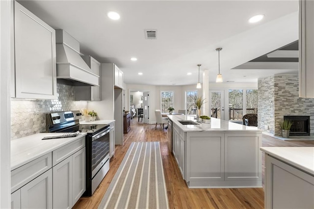 kitchen with visible vents, backsplash, custom range hood, stainless steel range with electric cooktop, and a sink