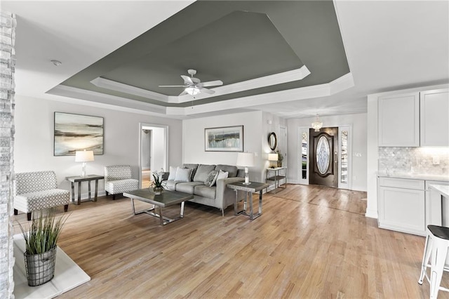 living area featuring a tray ceiling, crown molding, light wood-style floors, and ceiling fan