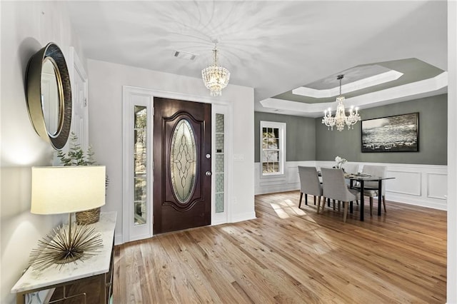 foyer entrance featuring visible vents, wood finished floors, an inviting chandelier, a decorative wall, and a raised ceiling