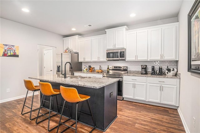kitchen featuring a center island with sink, visible vents, white cabinets, appliances with stainless steel finishes, and a breakfast bar area