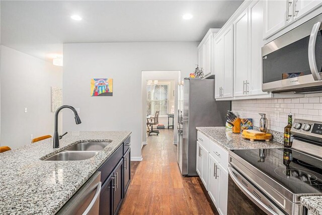 kitchen featuring stainless steel appliances, backsplash, white cabinetry, a sink, and wood finished floors