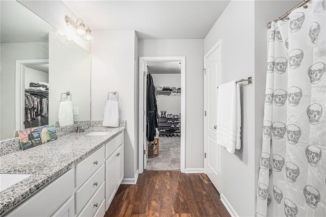 full bath with double vanity, baseboards, wood finished floors, a walk in closet, and a sink