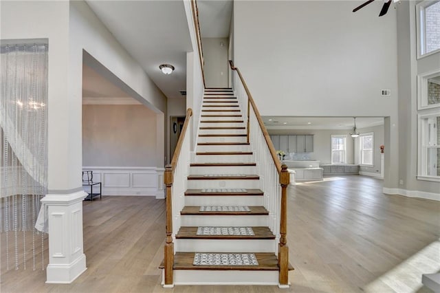 stairs featuring a decorative wall, wood finished floors, a ceiling fan, wainscoting, and decorative columns