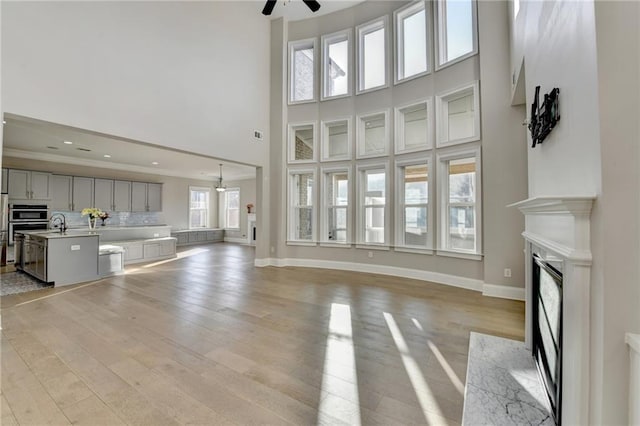 unfurnished living room featuring light wood finished floors, ceiling fan, a premium fireplace, and baseboards