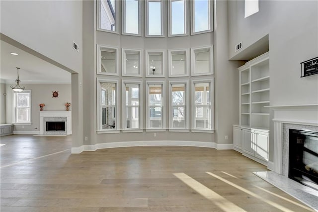 unfurnished living room with a high ceiling, light wood finished floors, a premium fireplace, and baseboards