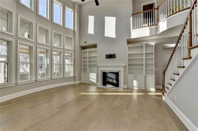 unfurnished living room with stairway, baseboards, wood finished floors, and a glass covered fireplace