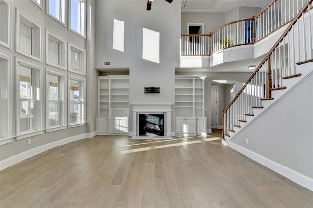 unfurnished living room featuring a glass covered fireplace, wood finished floors, a towering ceiling, and baseboards