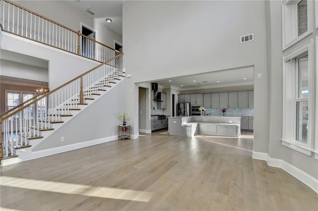 unfurnished living room featuring visible vents, stairway, a towering ceiling, light wood-style flooring, and baseboards