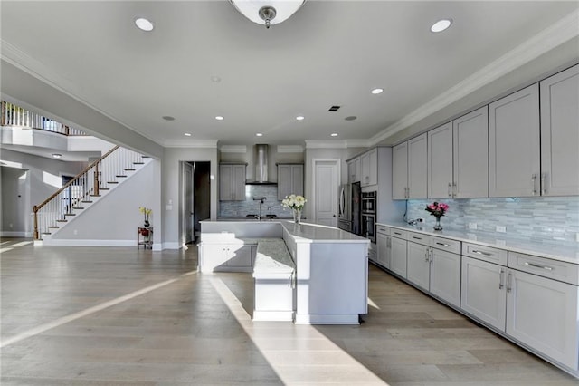 kitchen featuring wall chimney exhaust hood, ornamental molding, freestanding refrigerator, gray cabinetry, and light wood-type flooring