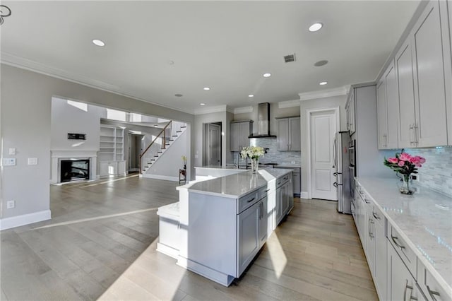 kitchen featuring gray cabinetry, a fireplace, visible vents, wall chimney range hood, and freestanding refrigerator