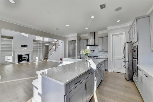 kitchen with gray cabinetry, visible vents, a fireplace, and wall chimney exhaust hood