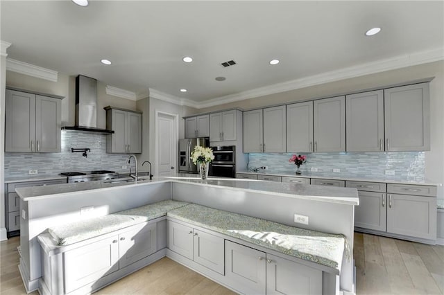 kitchen featuring gray cabinets, visible vents, appliances with stainless steel finishes, a sink, and wall chimney range hood