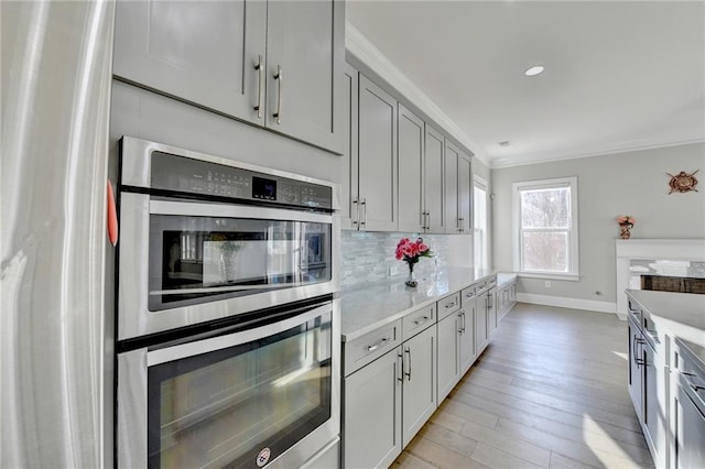 kitchen with crown molding, light wood finished floors, stainless steel appliances, light countertops, and backsplash