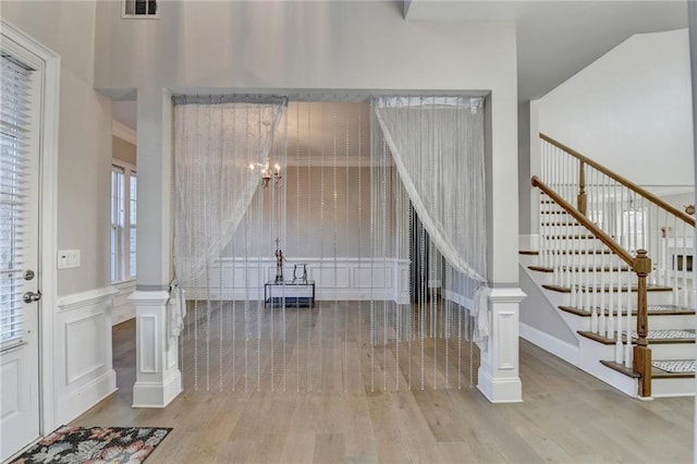 foyer featuring a wainscoted wall, visible vents, a decorative wall, wood finished floors, and stairs