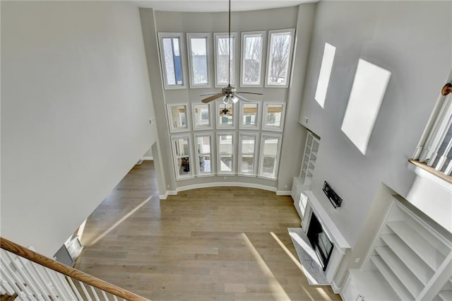 unfurnished living room with baseboards, a high ceiling, ceiling fan, and light wood finished floors