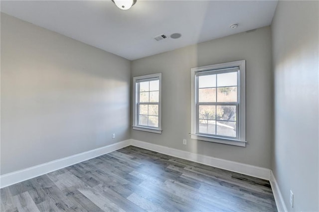 spare room featuring wood finished floors, visible vents, and baseboards