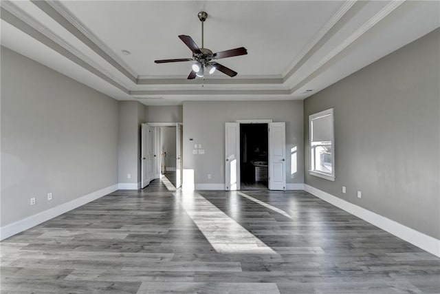 unfurnished bedroom featuring baseboards, a tray ceiling, crown molding, and wood finished floors