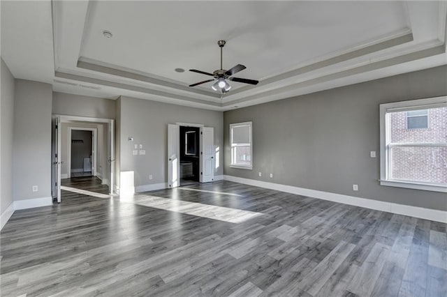 unfurnished room with a tray ceiling, wood finished floors, and baseboards