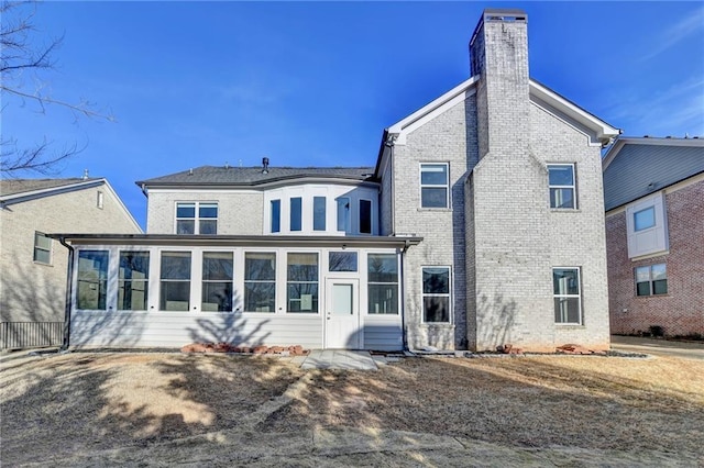 rear view of house featuring brick siding, a chimney, and a sunroom