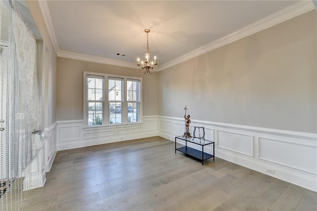 spare room with crown molding, visible vents, a decorative wall, wood finished floors, and a chandelier