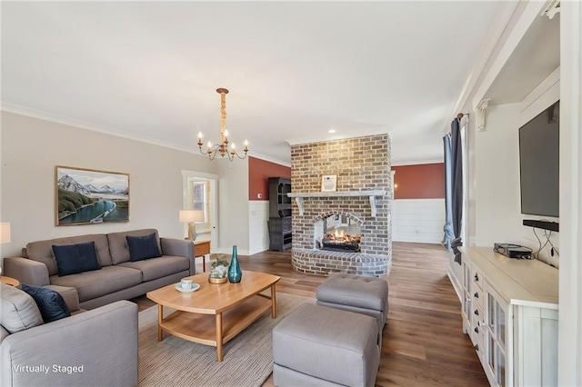 living room with wood finished floors, a notable chandelier, a brick fireplace, and ornamental molding