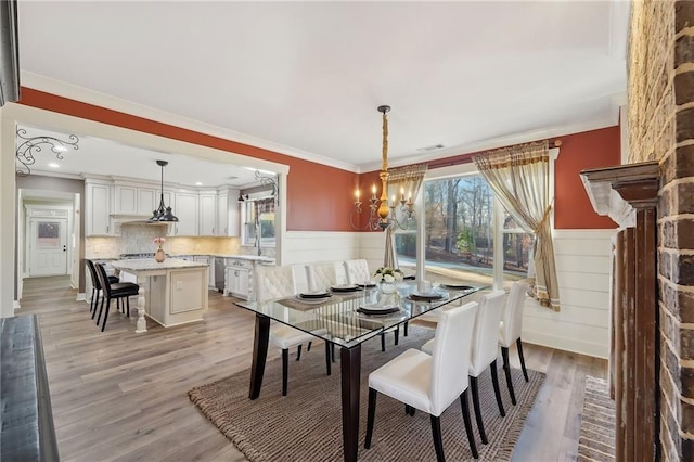 dining room with a wainscoted wall, light wood-style flooring, an inviting chandelier, and ornamental molding