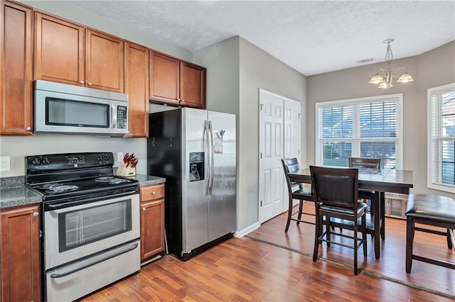 kitchen featuring a textured ceiling, stainless steel appliances, dark wood-type flooring, pendant lighting, and a chandelier