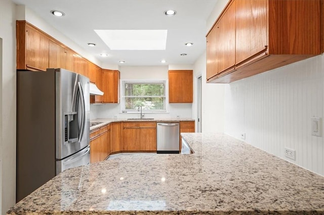 kitchen featuring a skylight, stainless steel appliances, under cabinet range hood, a sink, and light stone counters