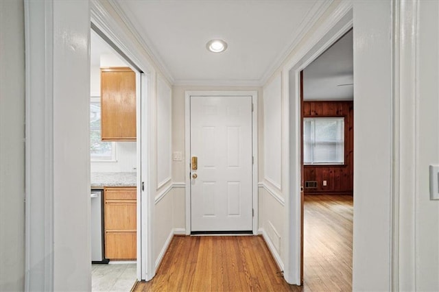 hallway with crown molding, wooden walls, and light wood-type flooring