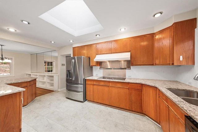 kitchen featuring under cabinet range hood, a sink, a skylight, appliances with stainless steel finishes, and brown cabinetry