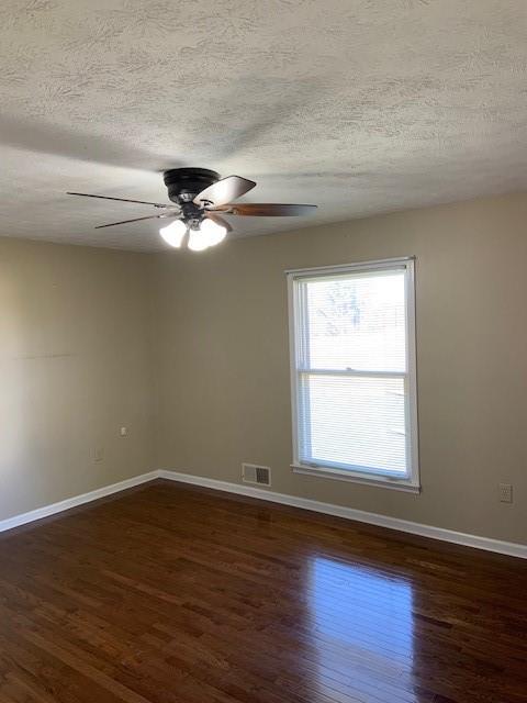 empty room featuring ceiling fan, dark wood-type flooring, and a textured ceiling