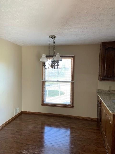 unfurnished dining area with dark wood-type flooring, an inviting chandelier, and a textured ceiling