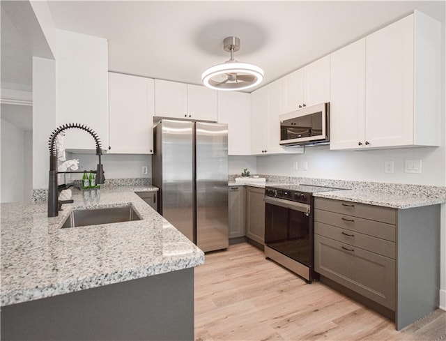 kitchen featuring light wood-type flooring, light stone counters, stainless steel dishwasher, and gray cabinetry