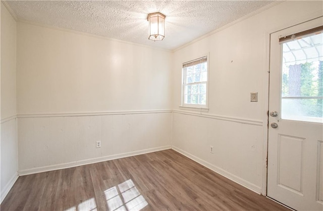 interior space featuring a wainscoted wall, crown molding, a textured ceiling, and wood finished floors