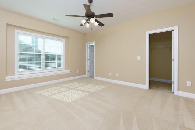 unfurnished bedroom featuring a spacious closet, light colored carpet, ceiling fan, and a closet