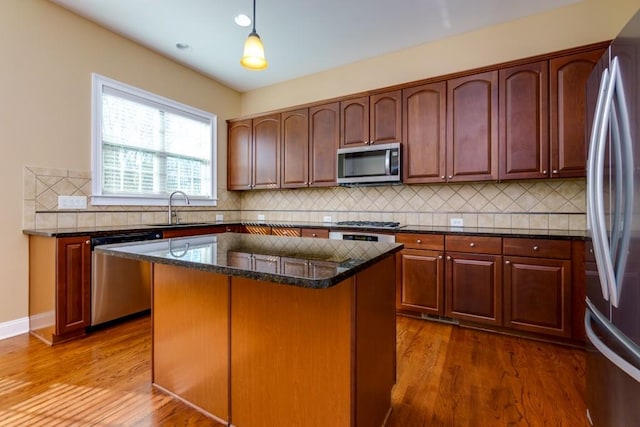 kitchen featuring sink, a center island, hanging light fixtures, dark stone countertops, and appliances with stainless steel finishes