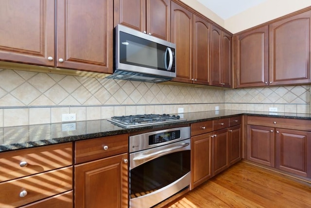 kitchen featuring stainless steel appliances, light hardwood / wood-style floors, decorative backsplash, and dark stone counters