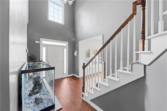 entrance foyer with a notable chandelier, a healthy amount of sunlight, wood-type flooring, and a towering ceiling