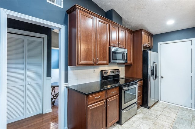 kitchen featuring appliances with stainless steel finishes, dark stone countertops, backsplash, and a textured ceiling