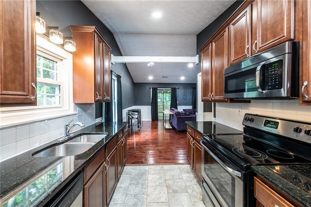 kitchen with sink, lofted ceiling, decorative backsplash, dark stone counters, and appliances with stainless steel finishes