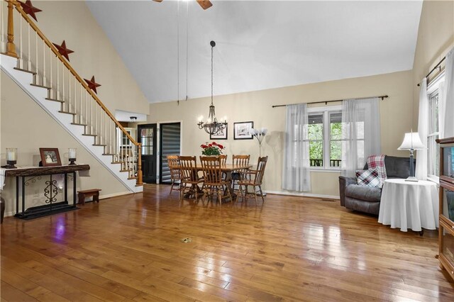 dining room featuring hardwood / wood-style flooring, baseboards, high vaulted ceiling, ceiling fan with notable chandelier, and stairs