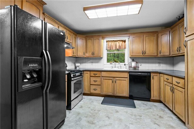 kitchen with dark countertops, tasteful backsplash, a sink, black appliances, and under cabinet range hood