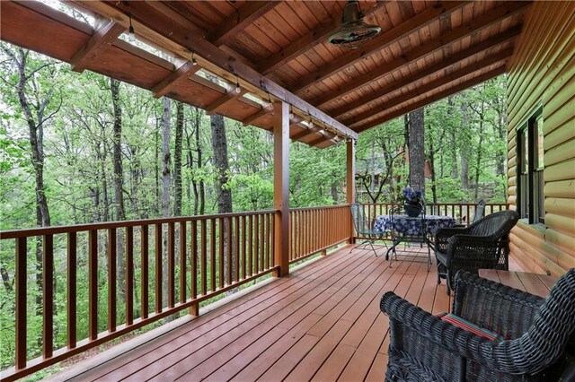 wooden terrace with a view of trees, outdoor dining space, and ceiling fan